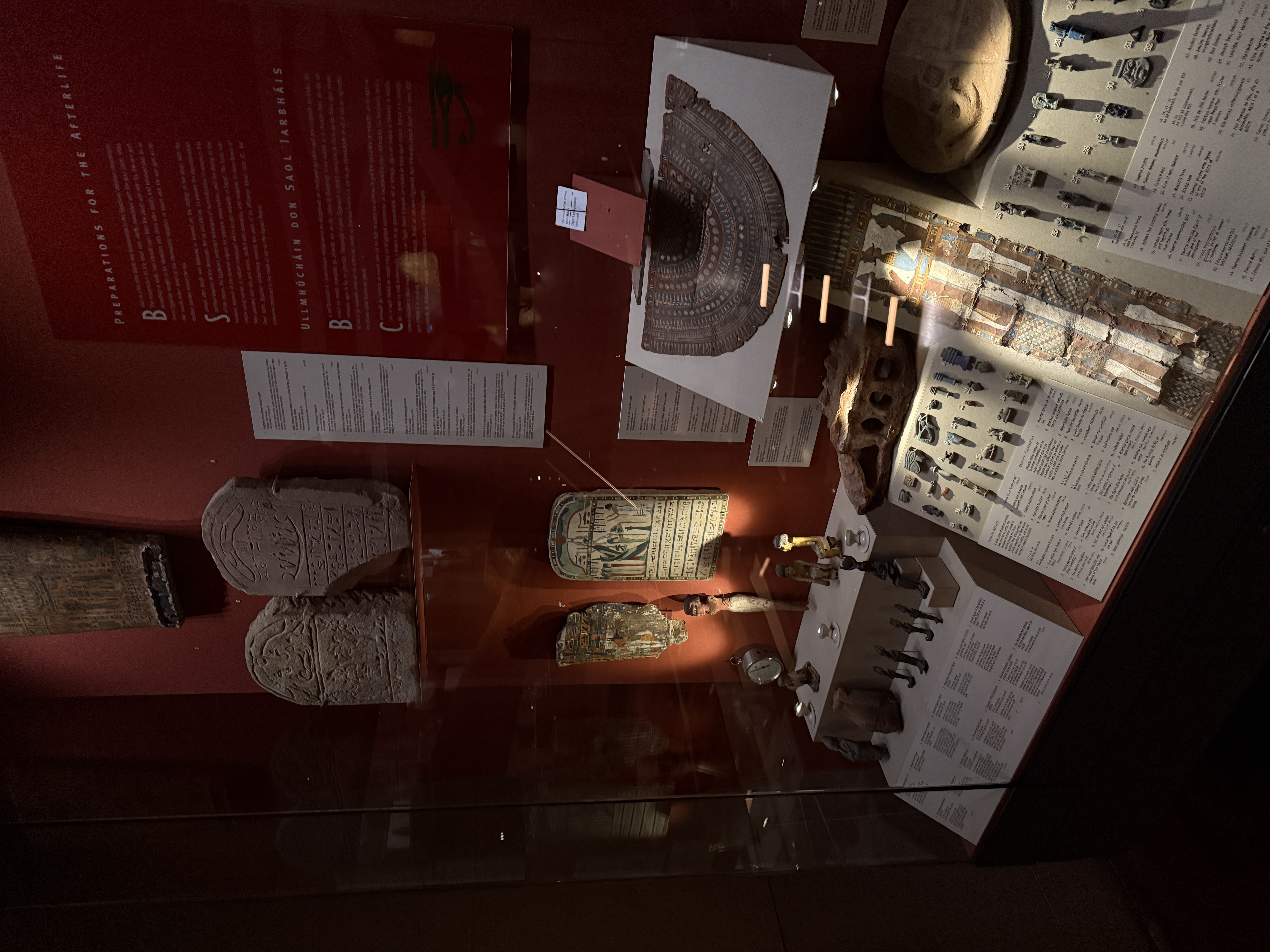 Decorative Egyptian artifacts in a display case. There are carvings on stone tablets and textiles